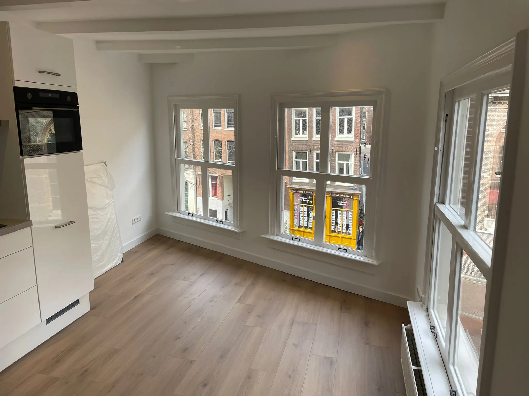 Lichte, lege kamer met houten vloer en uitzicht op de Korte Kolksteeg in een stadsomgeving.
